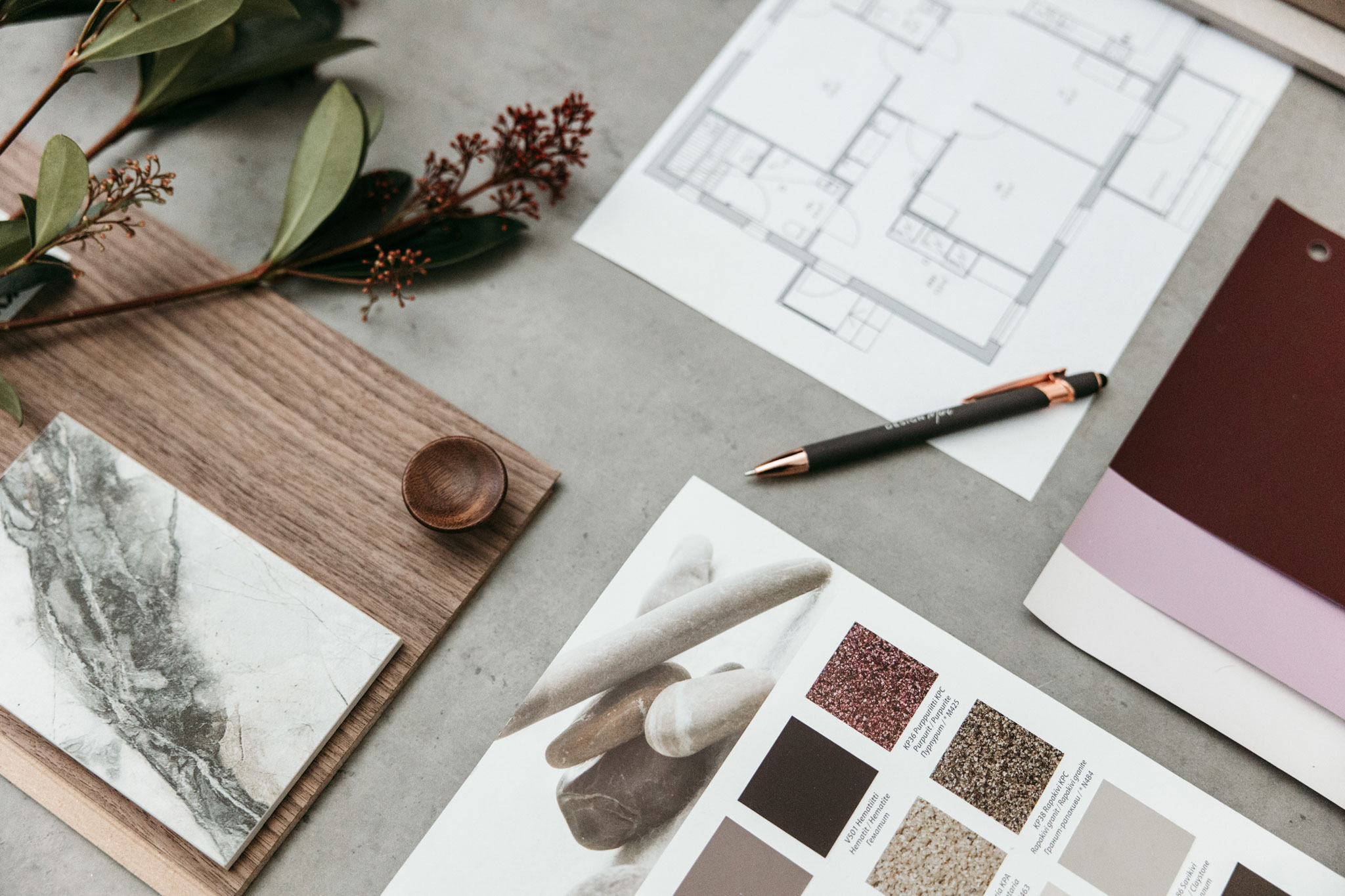 Sisustussuunnitteluun liittyvä työpöytä, jolla on pohjapiirros, sävynäytteitä ja luonnonmateriaaleja.