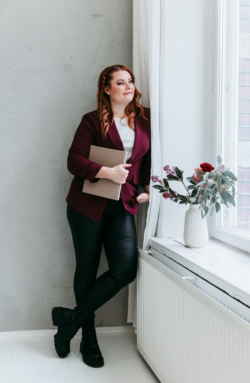 Sisustussuunnittelija Meri seisoo ikkunan ääressä kansio kädessään, jossa usein kysytyt kysymykset -sisältöä.